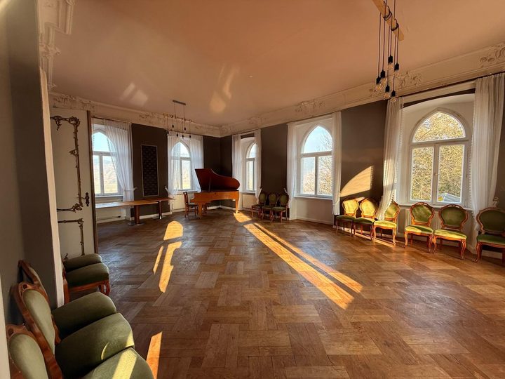Der Festsaal mit Flügel, Stuckdecke und Spitzbogenfenstern, Sonnenlicht auf dem Parkett