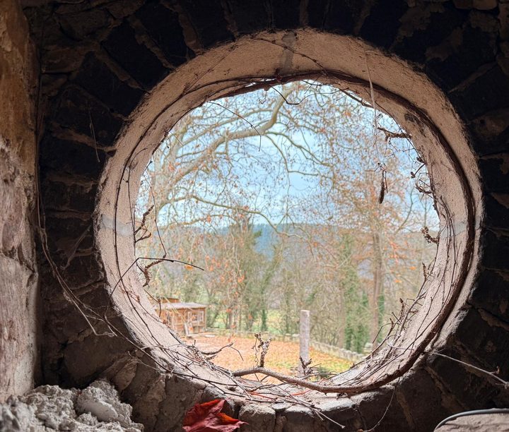 Rundes Fenster in der dicken Bruchsteinmauer, Blick hinaus in den winterlichen Garten