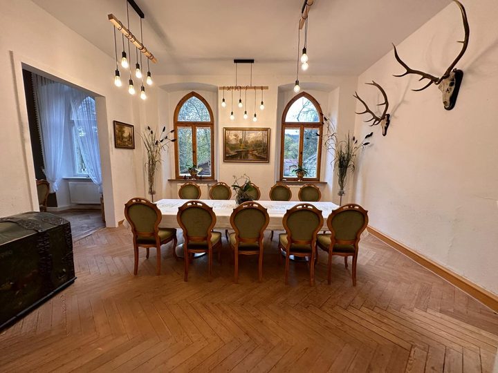 Lange weiß gedeckte Tafel im Speisesaal, an der Wand Geweihe, Spitzbogenfenster