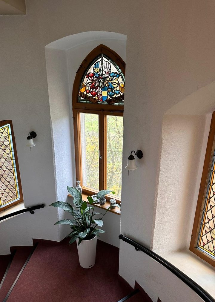 Treppenhaus mit Spitzbogenfenster, darin ein farbiges Wappen aus Bleiglas