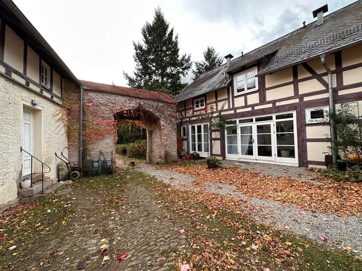 Der Wirtschaftshof im Herbst: Fachwerkgebäude, berankter Torbogen, Laub auf dem Pflaster
