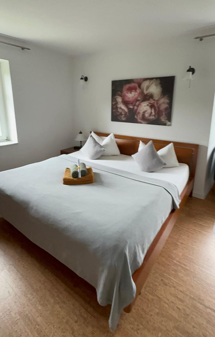 Helles Doppelzimmer im Forsthaus, über dem Bett ein Rosenbild, Handtücher bereitgelegt